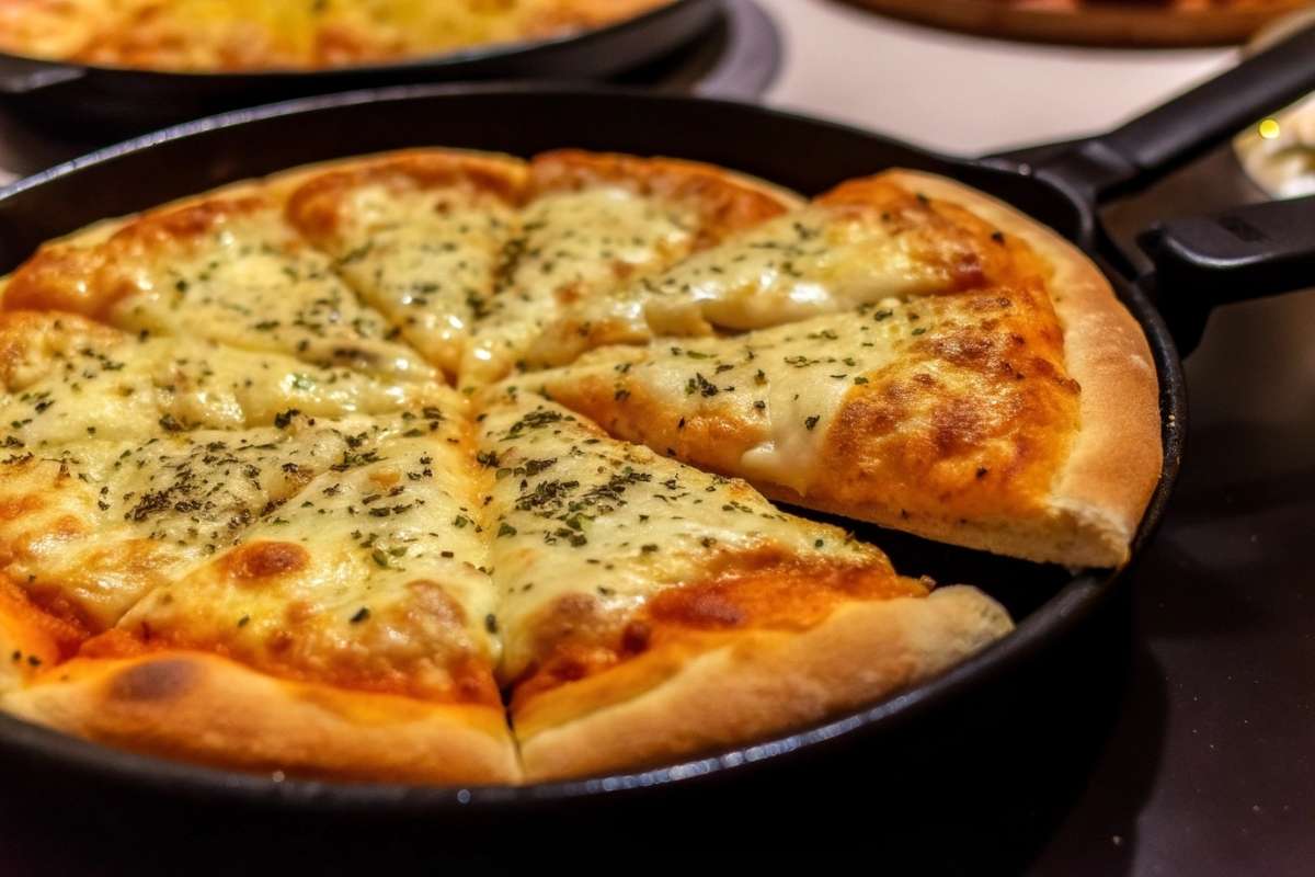 A cheesy pizza with a golden crust, topped with herbs, served in a cast-iron pan.