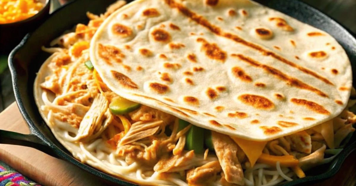 Close-up of a chicken quesadilla cooking on a skillet with shredded chicken, melted cheese, and vegetables.