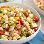 A fresh and colorful Chicken Avocado Salad with cherry tomatoes, cucumbers, and diced chicken in a white bowl.