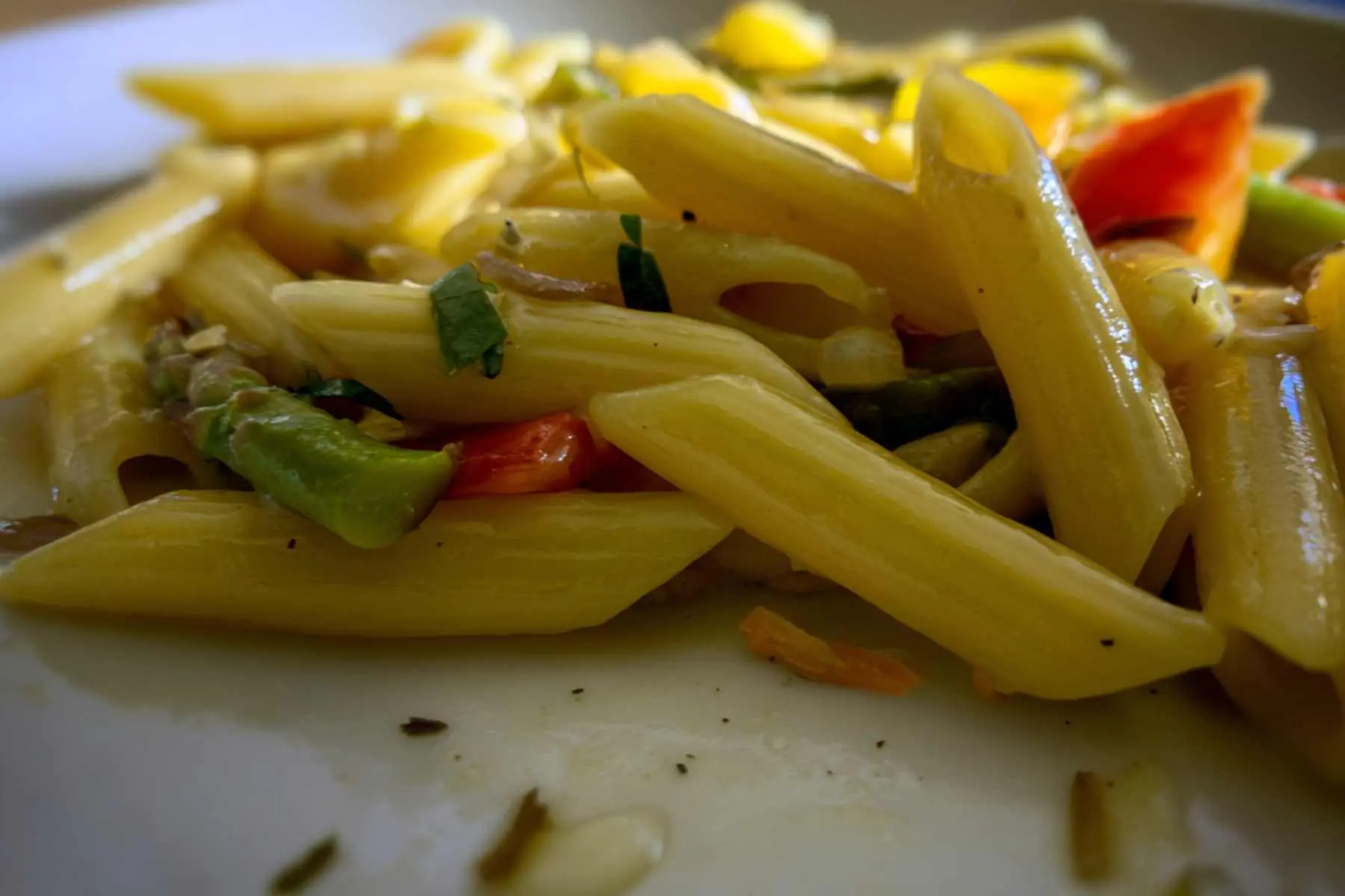 Pasta primavera cooks in a skillet with mixed vegetables and spaghetti. Steam rises lightly from the pan in a home kitchen.